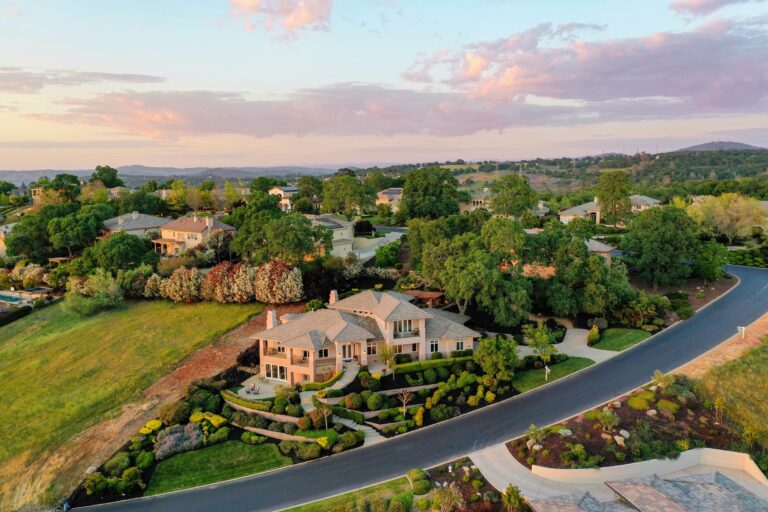 Aerial shot of elegant suburban houses with lush gardens during sunset.